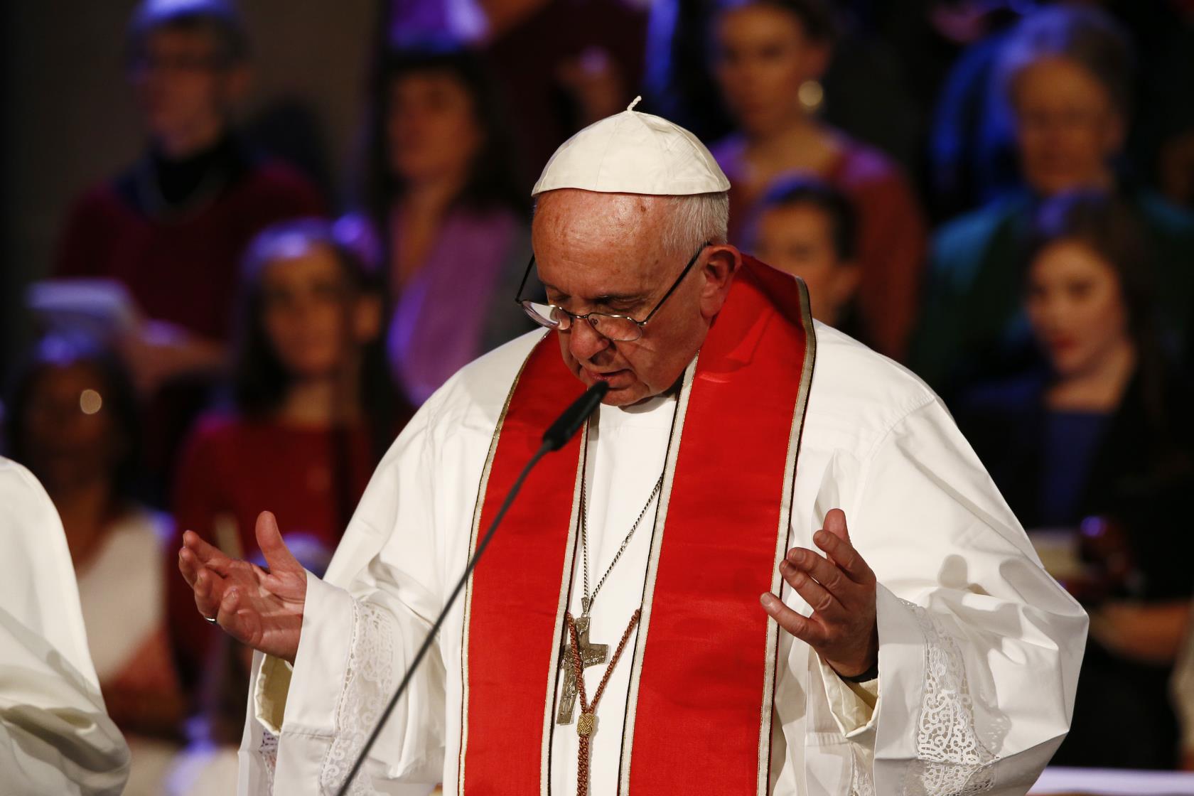 Påve Franciskus står med öpnade händer och säger något i en mikrofon.