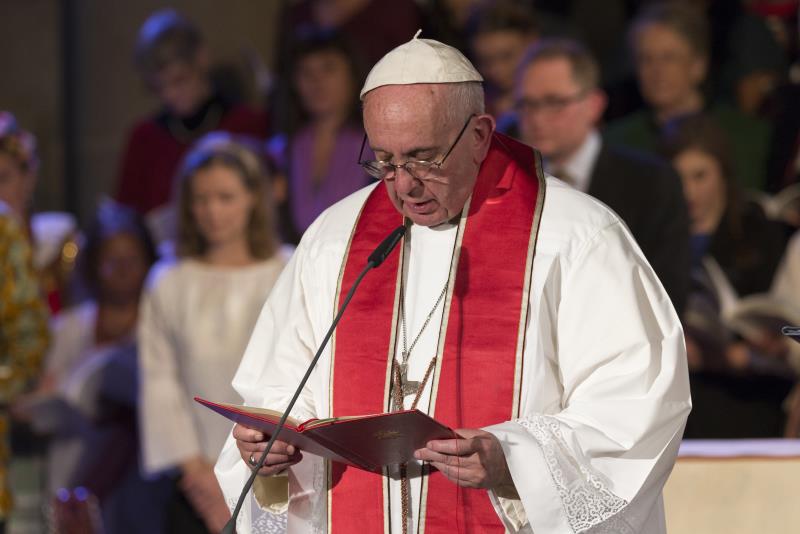 Påven Franciskus i vit kåpa och röd stola läser högt ur en bok.