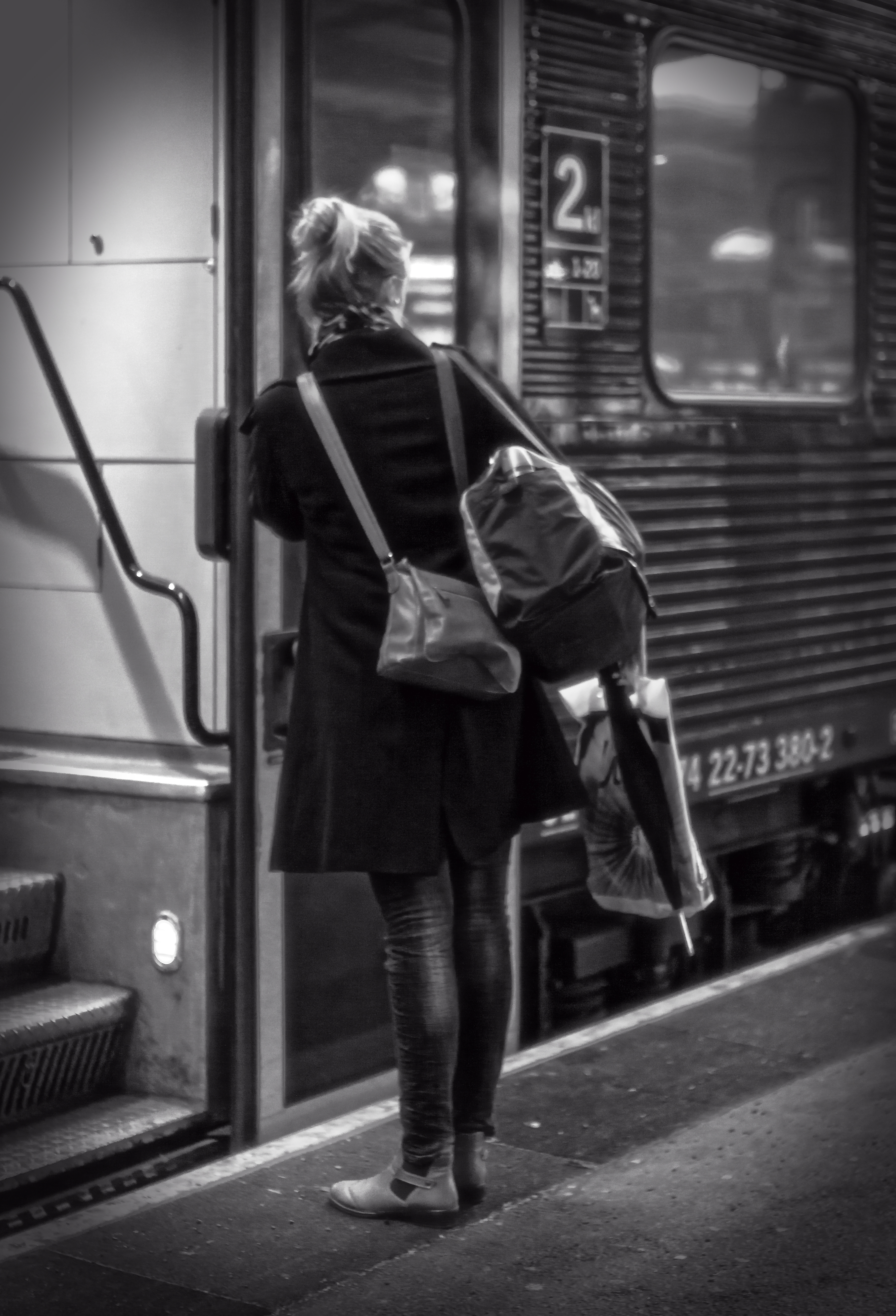 Svartvit bild på en kvinna som ska kliva på ett tåg från perrongen.