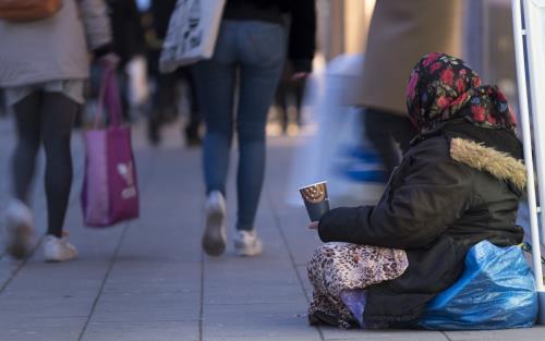 En tiggande kvinna i sjal sitter på marken med en kopp i handen.