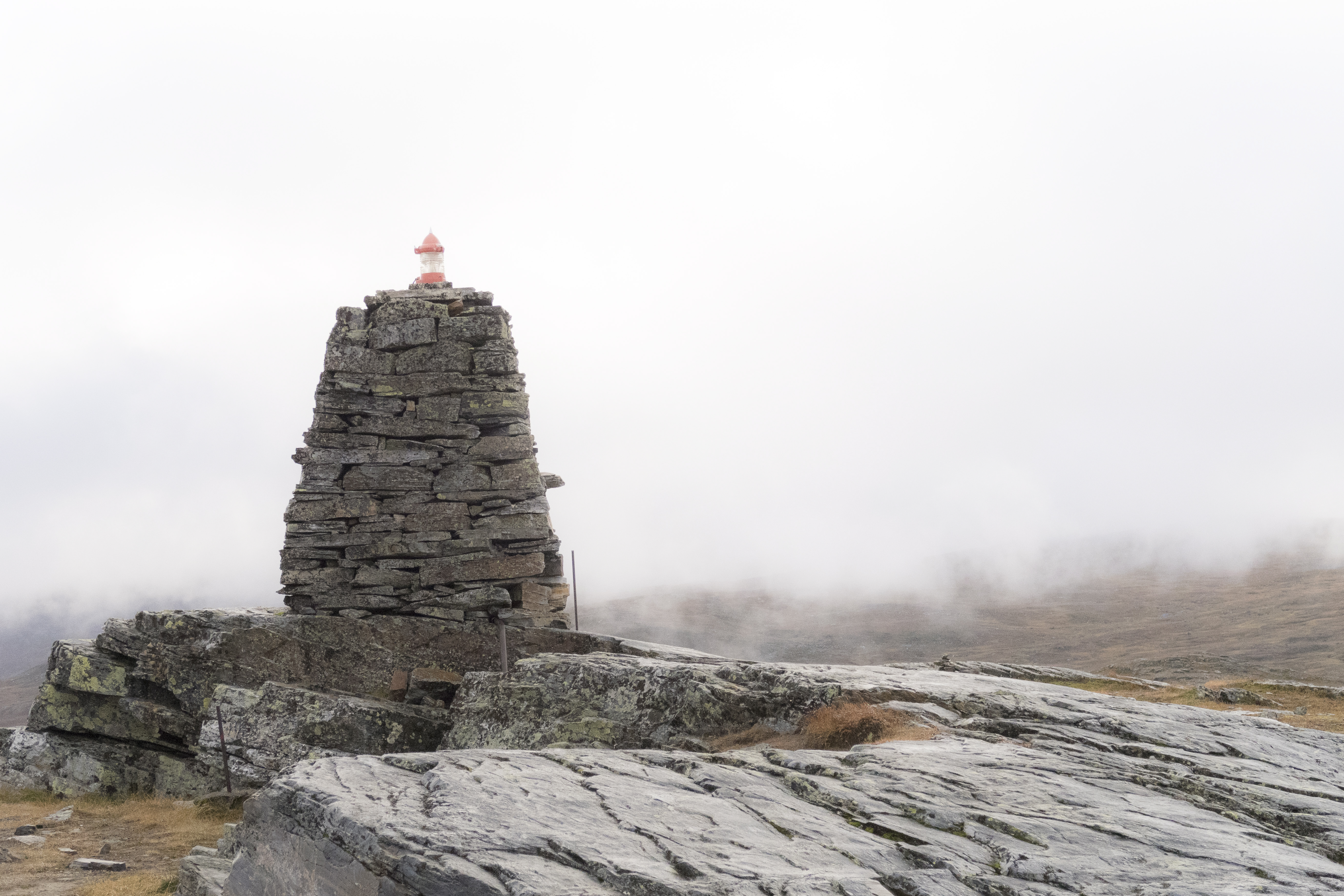 Ett stenröse på en fjälltopp, med en stormlykta högst upp. Dimma i bakgrunden.