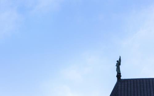 En änglastaty på ett tak mot blå himmel.