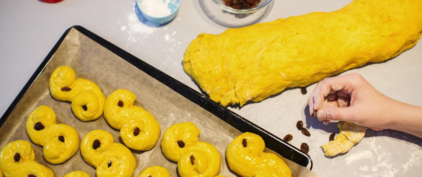 Någon stoppar russin i ogräddade lussebullar på en plåt.