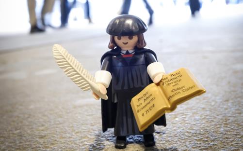 Martin Luther som legofigur står på marken. Människor rör sig runt om.