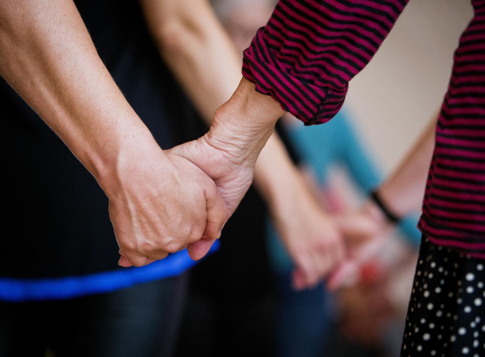 Närbild på två personer som håller hand. I bakgrunden håller fler par varandra i hand.