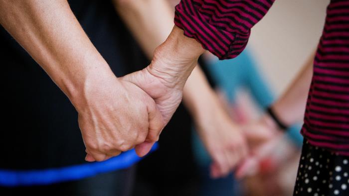 Närbild på två personer som håller hand. I bakgrunden håller fler par varandra i hand.