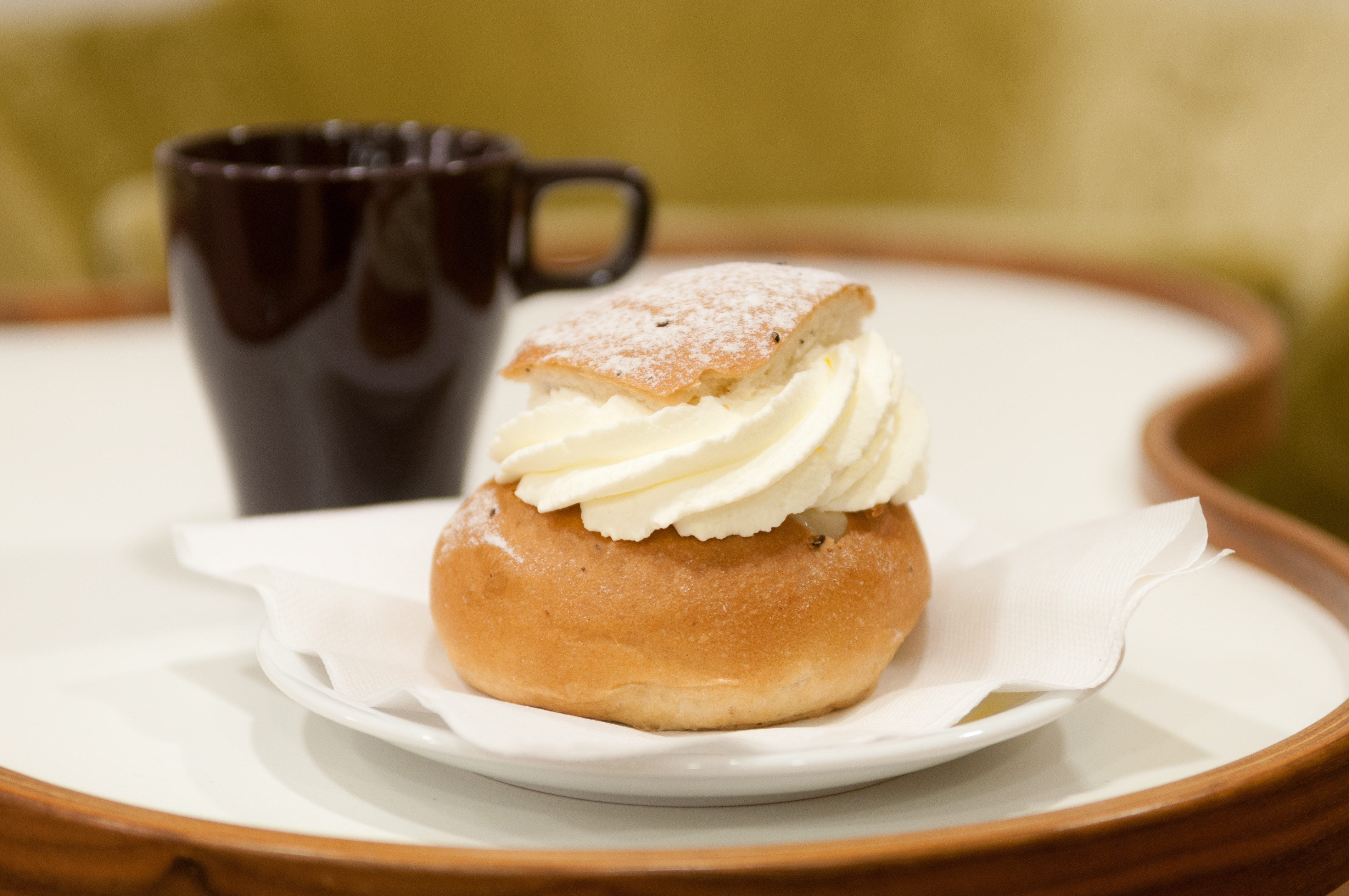 En semla och en kaffekopp står serverat på ett bord.