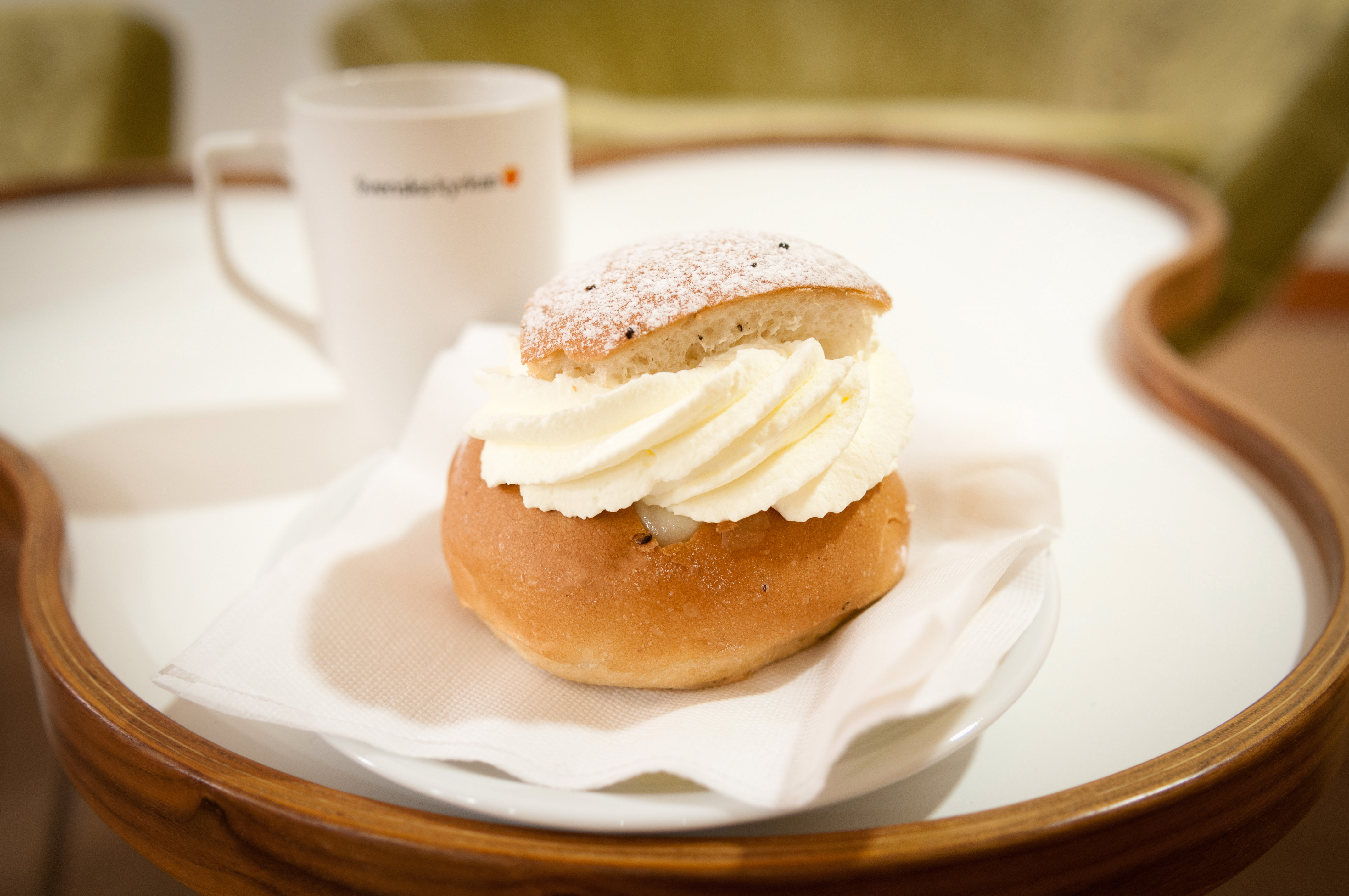 En semla och en kaffekopp står serverat på ett bord.
