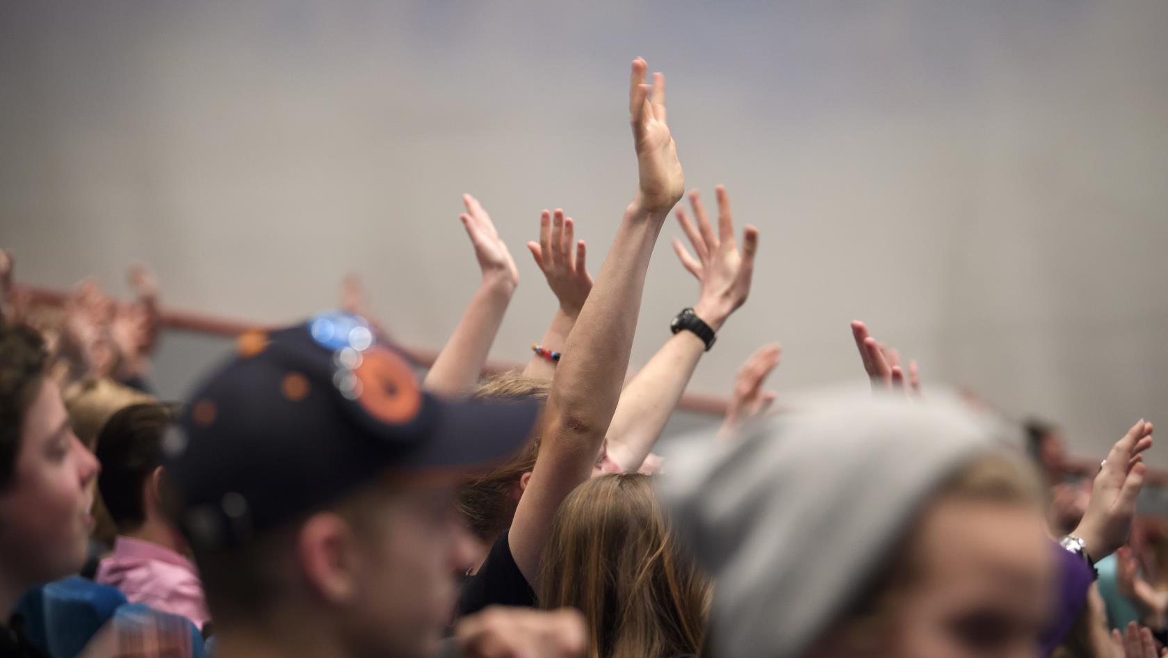 En stor grupp med ungdomar sträcker upp händerna i luften.