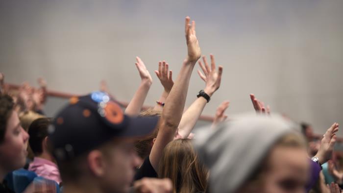 En stor grupp med ungdomar sträcker upp händerna i luften.