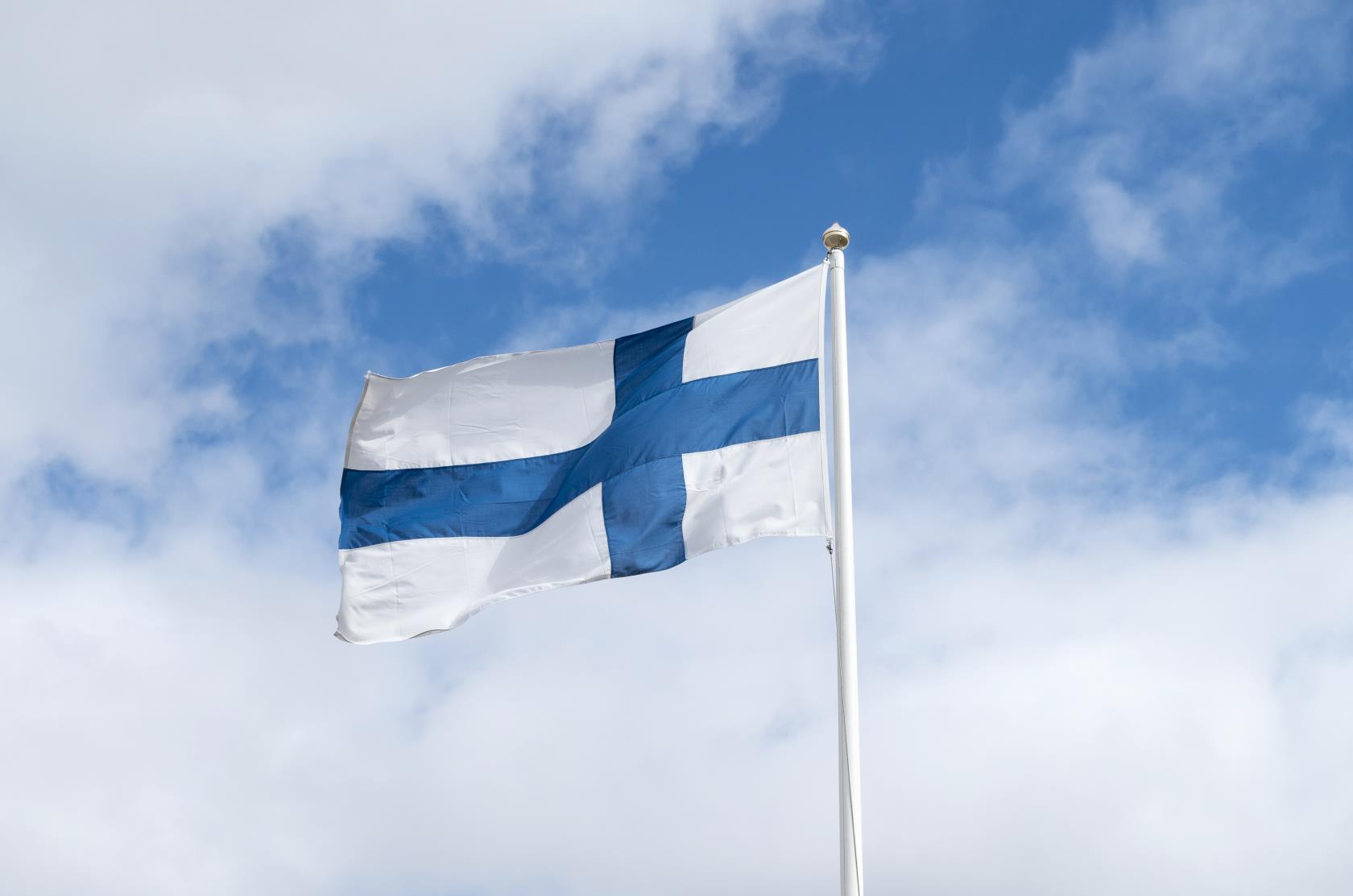En flaggstång med finska flaggan mot en blå och molnig himmel.