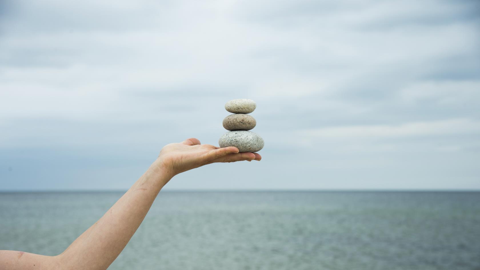 Någon står vid vattnet och balanser tre stenar på varandra i handen.