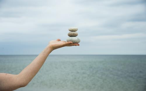 Någon står vid vattnet och balanser tre stenar på varandra i handen.