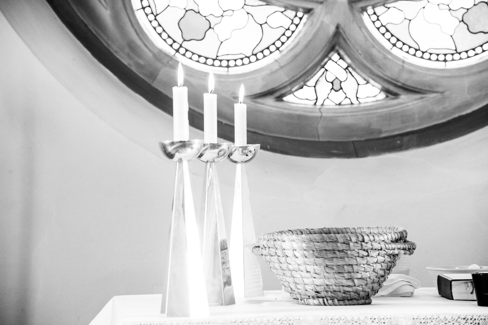 En svartvit bild av tre ljusstakar och en korg på ett altare.