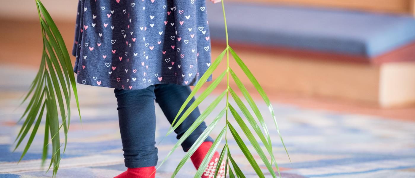 Ett barn i strumplästen går med palmblad i händerna.
