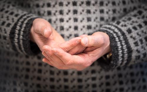 Någon håller händerna kupade framför sig. Personen i fråga har en grov stickad tröja i svart och grått.