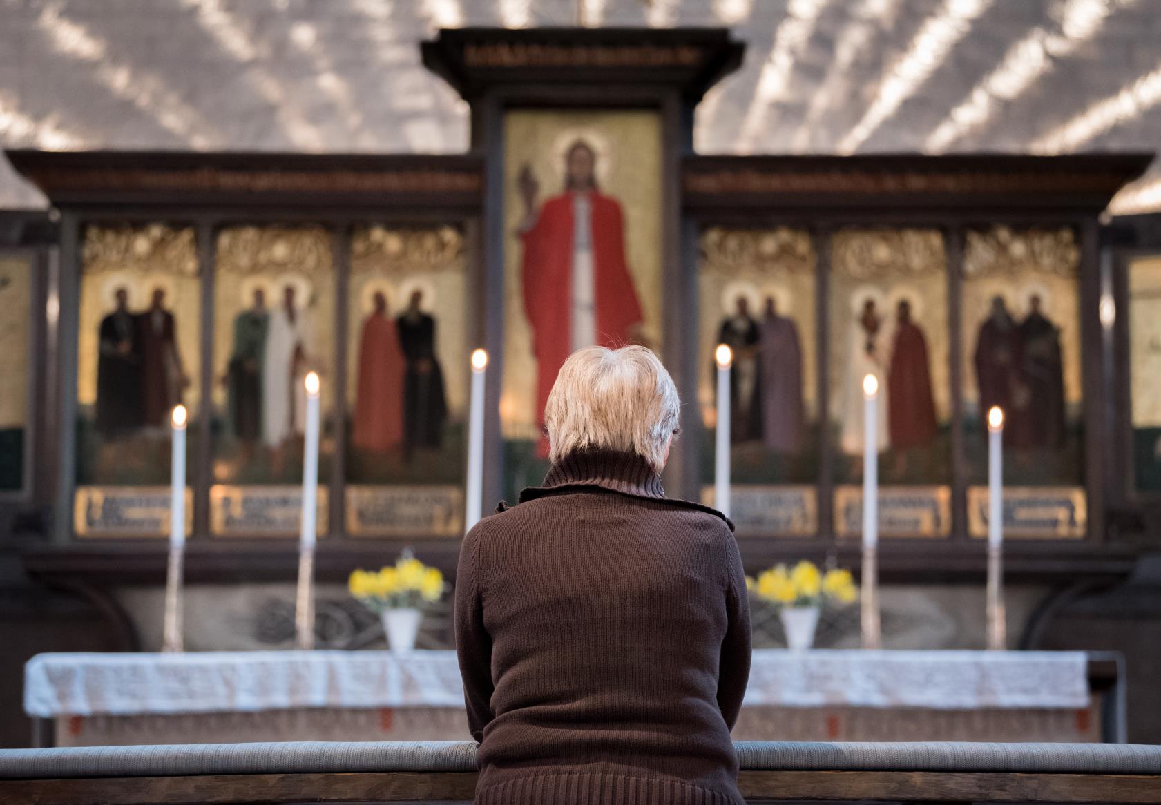En kvinna sitter framför ett altare med en stor altartavla.