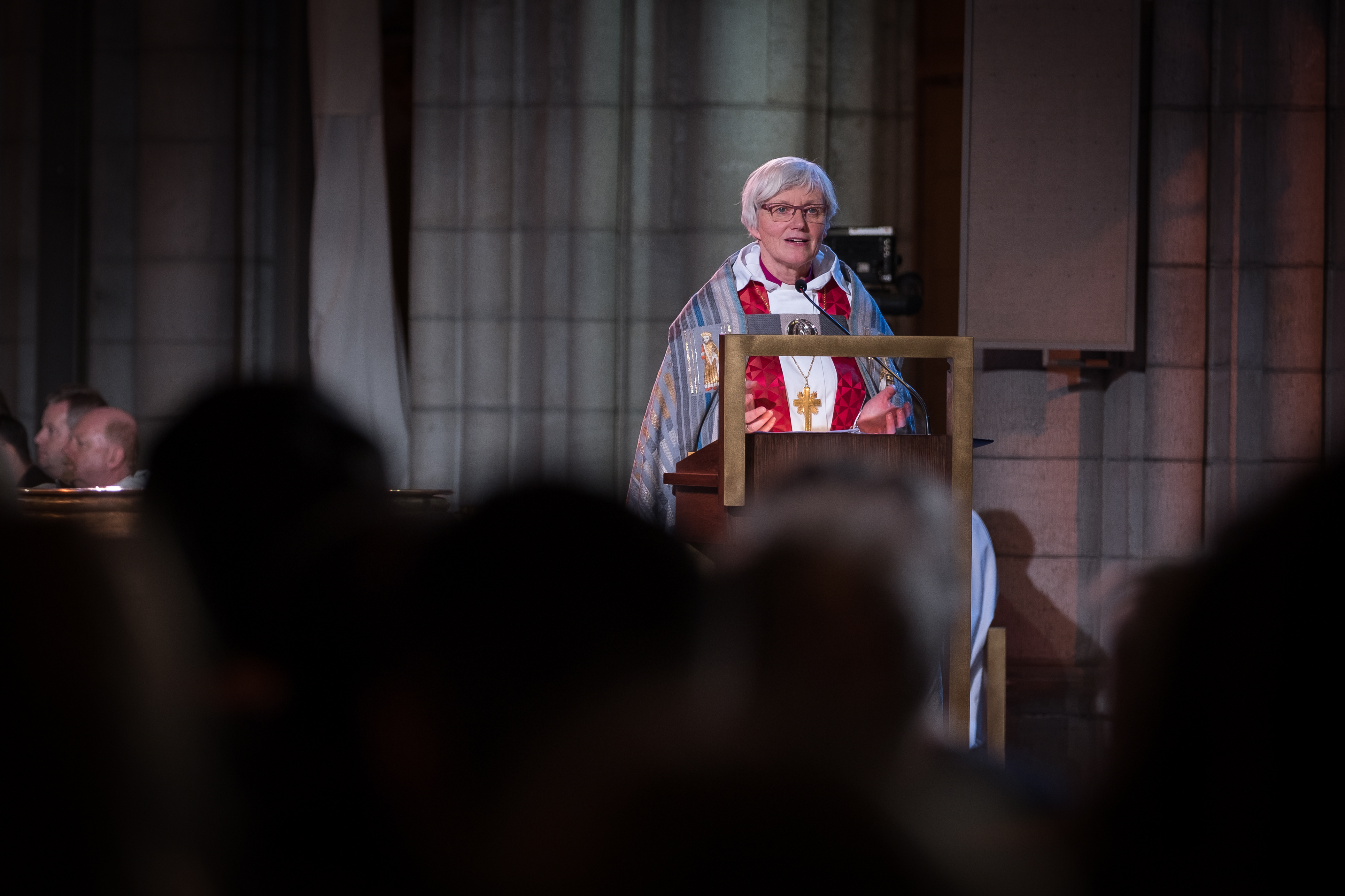 Ärkebiskop Antje Jackelén står i en talarstol i Uppsala domkyrka i ämbetsdräkt. Suddiga huvuden i förgrunden.