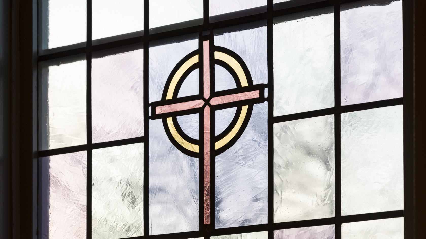 Närbild på ett färgat kyrkfönster med ett kors i mitten.
