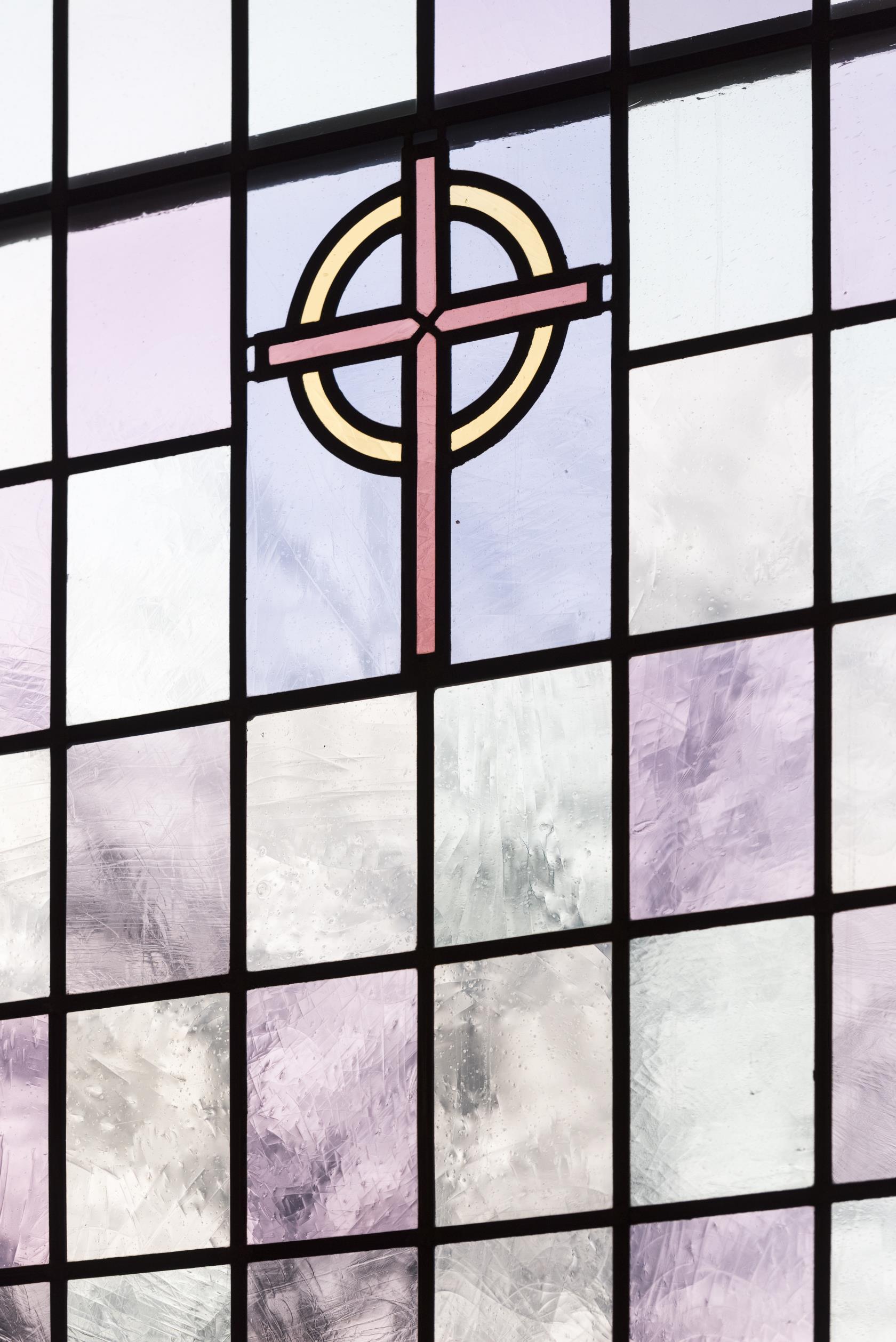 Närbild på ett färgat kyrkfönster med ett kors i mitten.