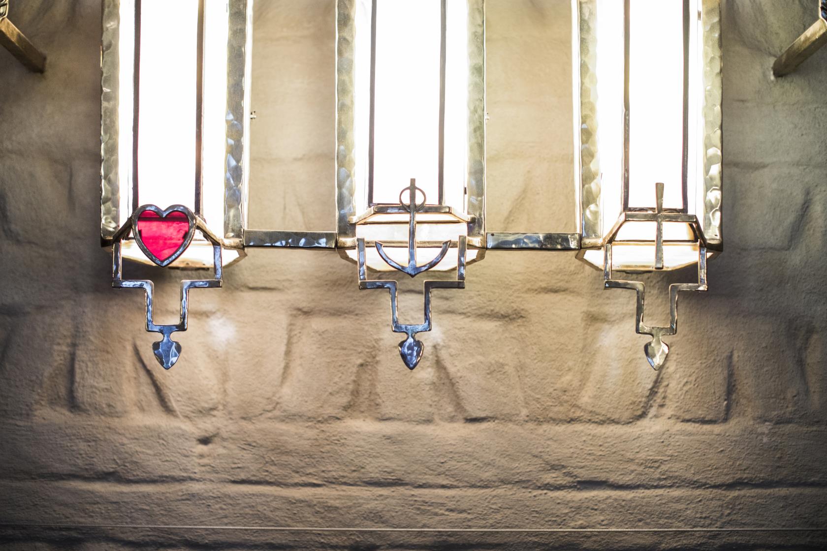 Framför tre smala kyrkfönster hänger i tur och ordning ett hjärta, ett ankare och ett kors.