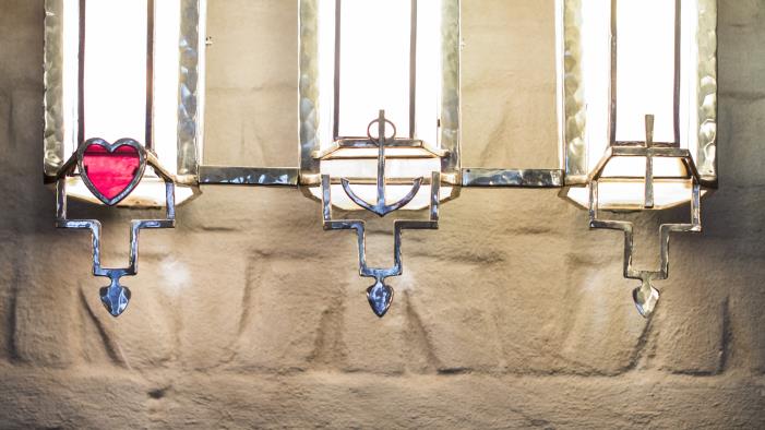 Framför tre smala kyrkfönster hänger i tur och ordning ett hjärta, ett ankare och ett kors.