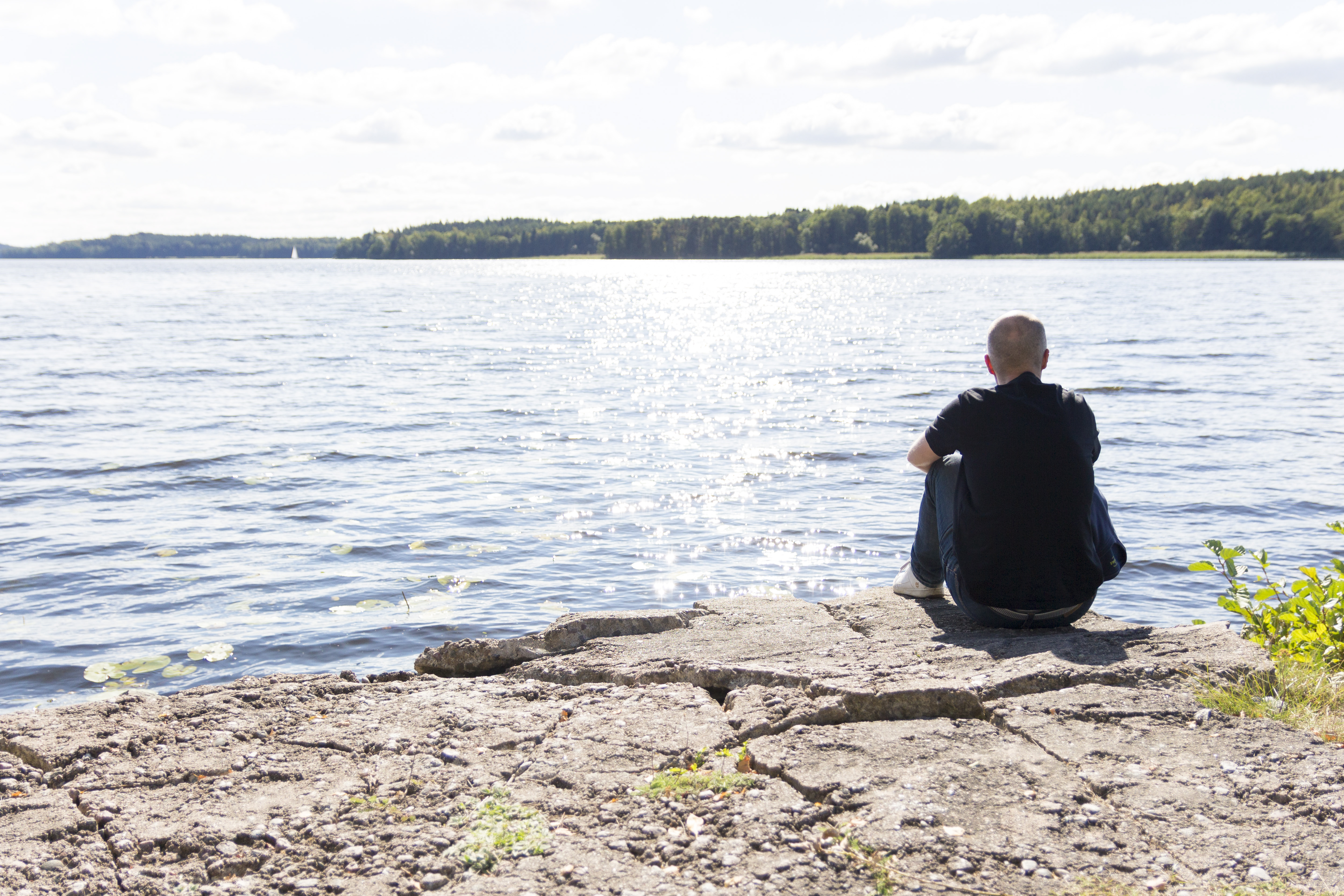 En man sitter på en klippa vid vattnet.