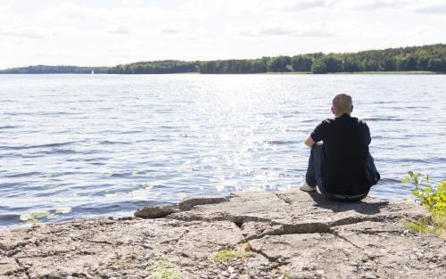 En man sitter på en klippa vid vattnet.