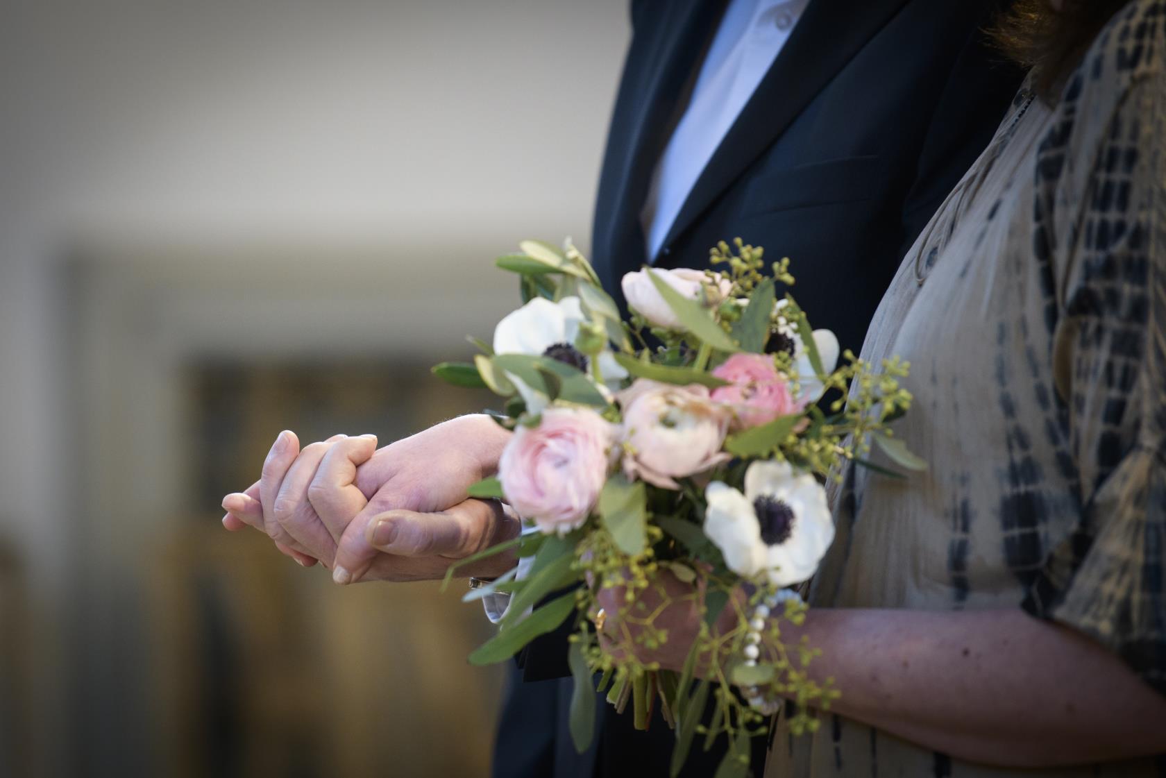 Ett brudpar håller hand. Bruden håller en bukett i andra handen.