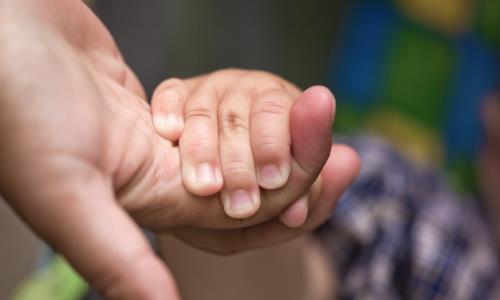 En liten barnhand håller om en vuxens finger.