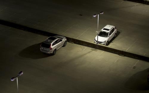 Två ensamma bilar i mörkret på en stor upplyst parkering.