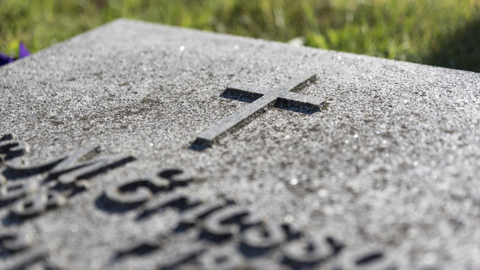 Närbild på en gravsten med ett kors.