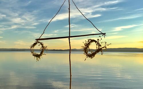 En midsommarstång med vissna kransar står vid vattnet.