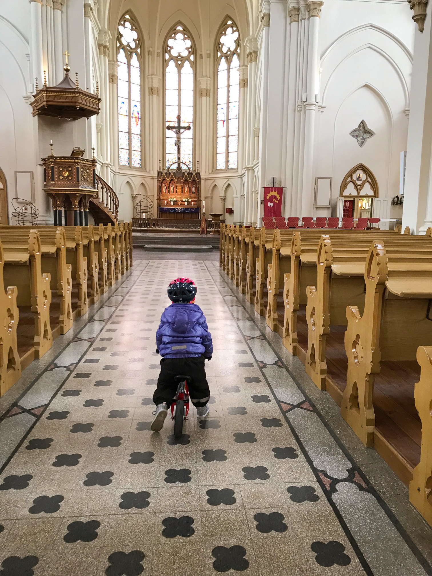 Ett litet barn cyklar i mittgången i en kyrka.