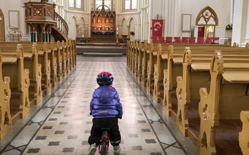 Ett litet barn cyklar i mittgången i en kyrka.