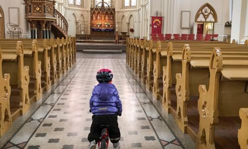 Ett litet barn cyklar i mittgången i en kyrka.