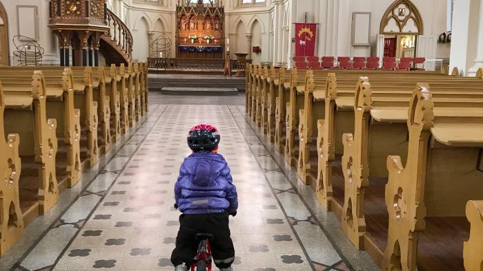 Ett litet barn cyklar i mittgången i en kyrka.