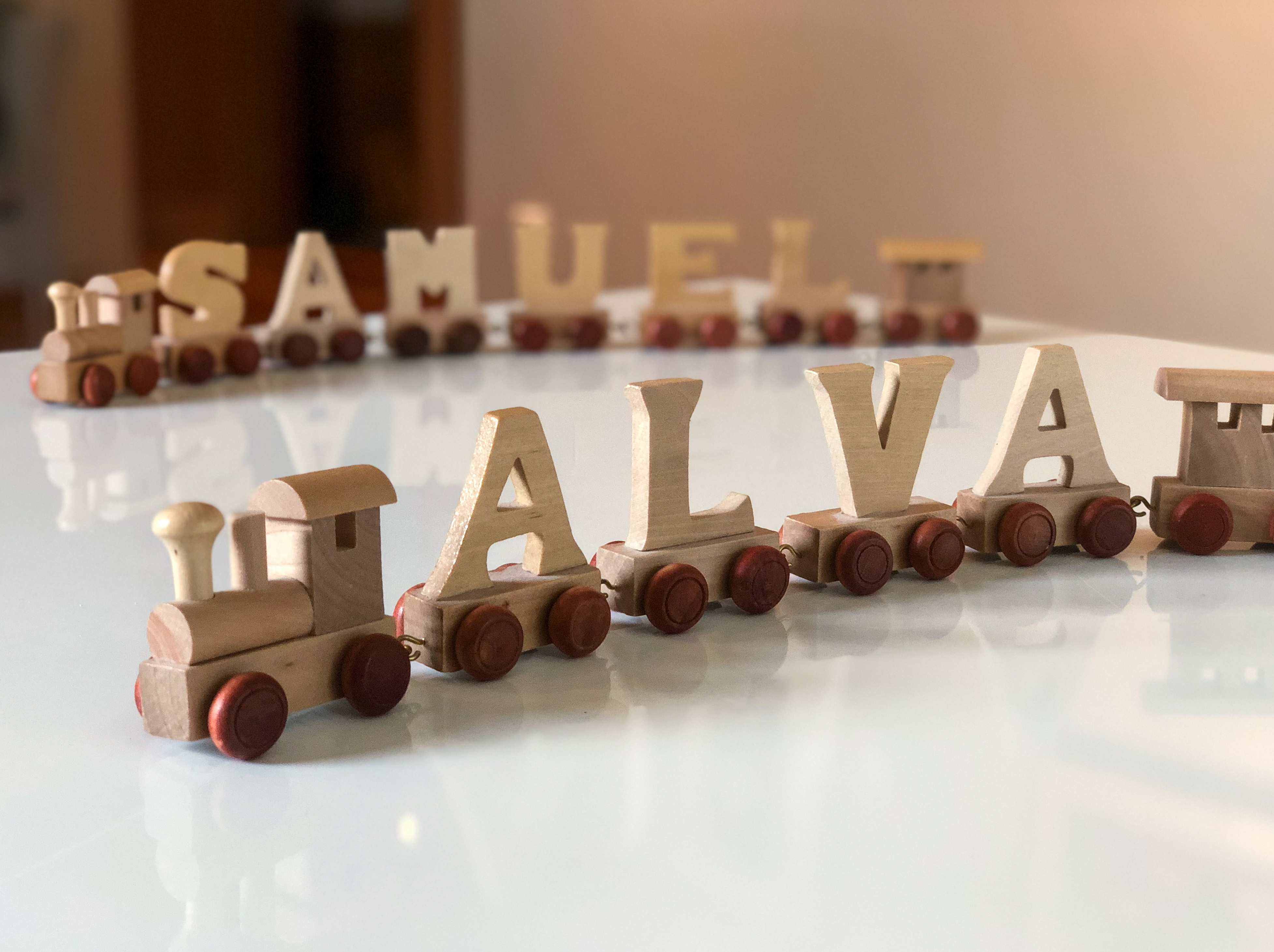 Två leksakståg med bokstäver på vagnarna som bildar namnen Samuel och Alva.