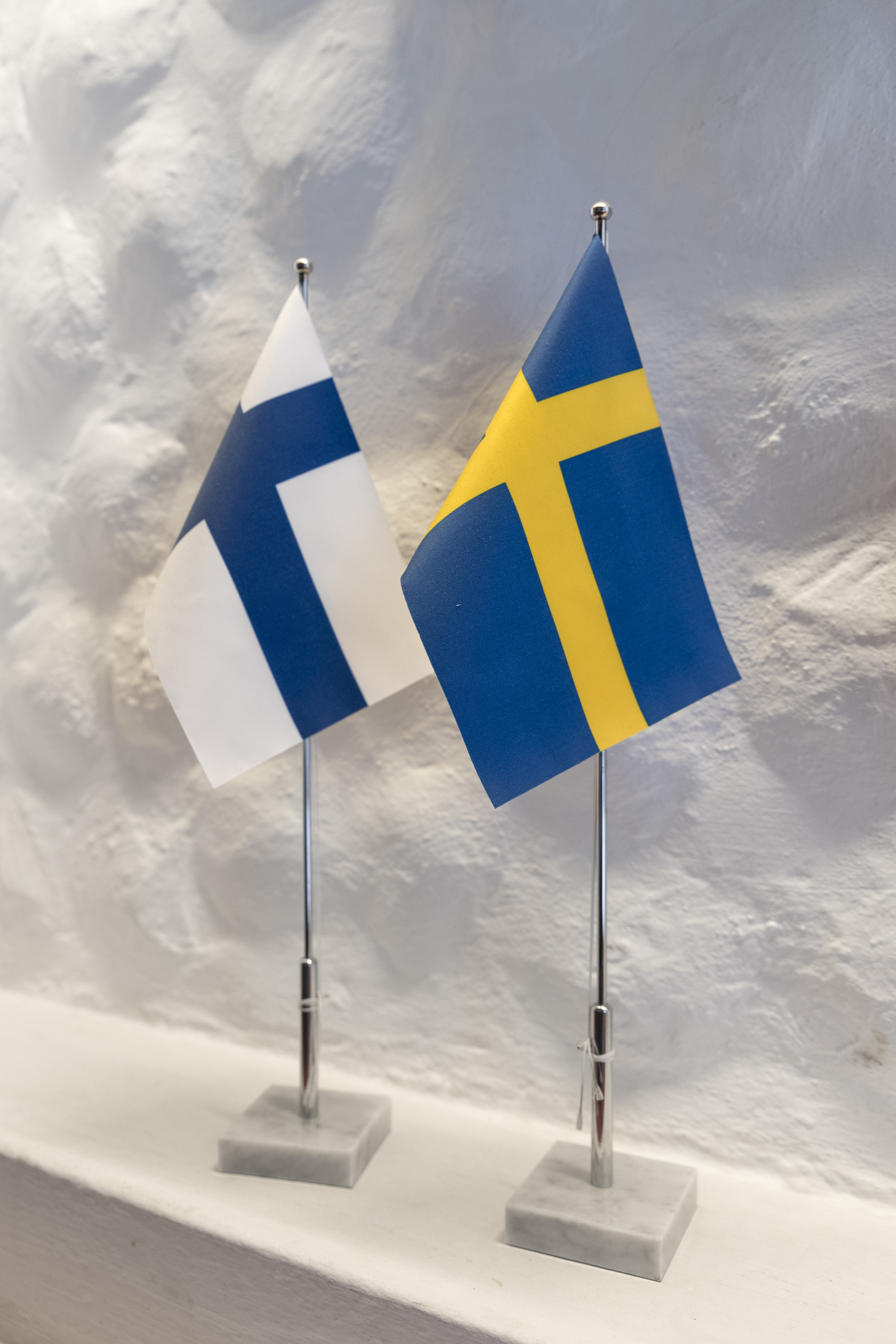 Två små flaggstänger med svenska och finska flaggan står på en hylla.
