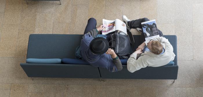 Två män fotograferade ovanifrån sitter i en soffa med varsin tidning.