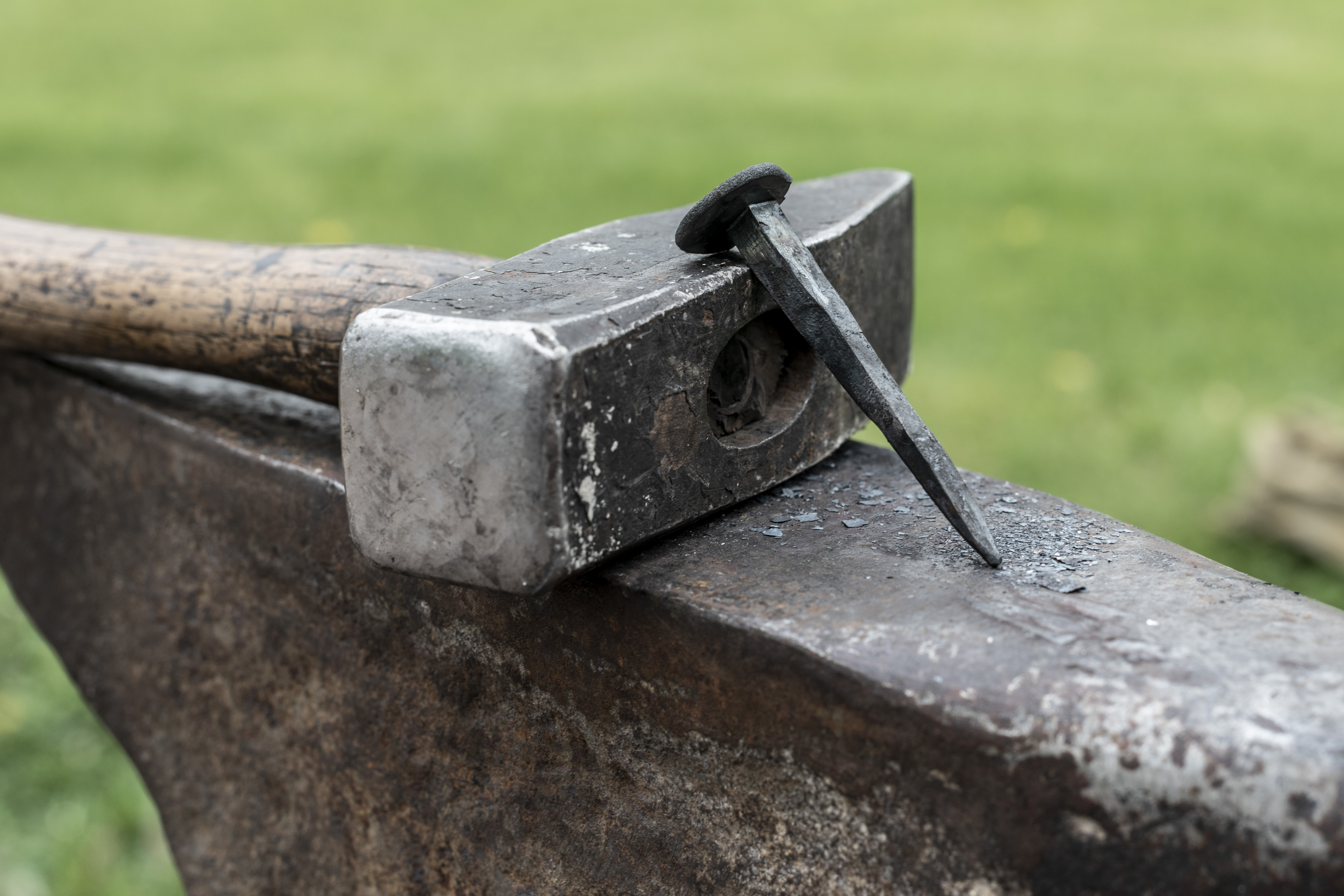 En hammare och en gammaldags spik ligger på ett städ.