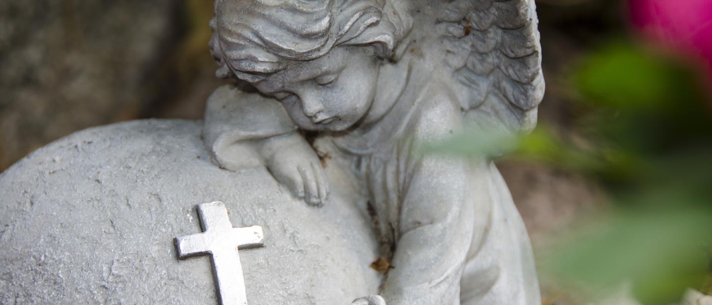 Närbild på en gravdekoration: en ängel kramar om en sten.