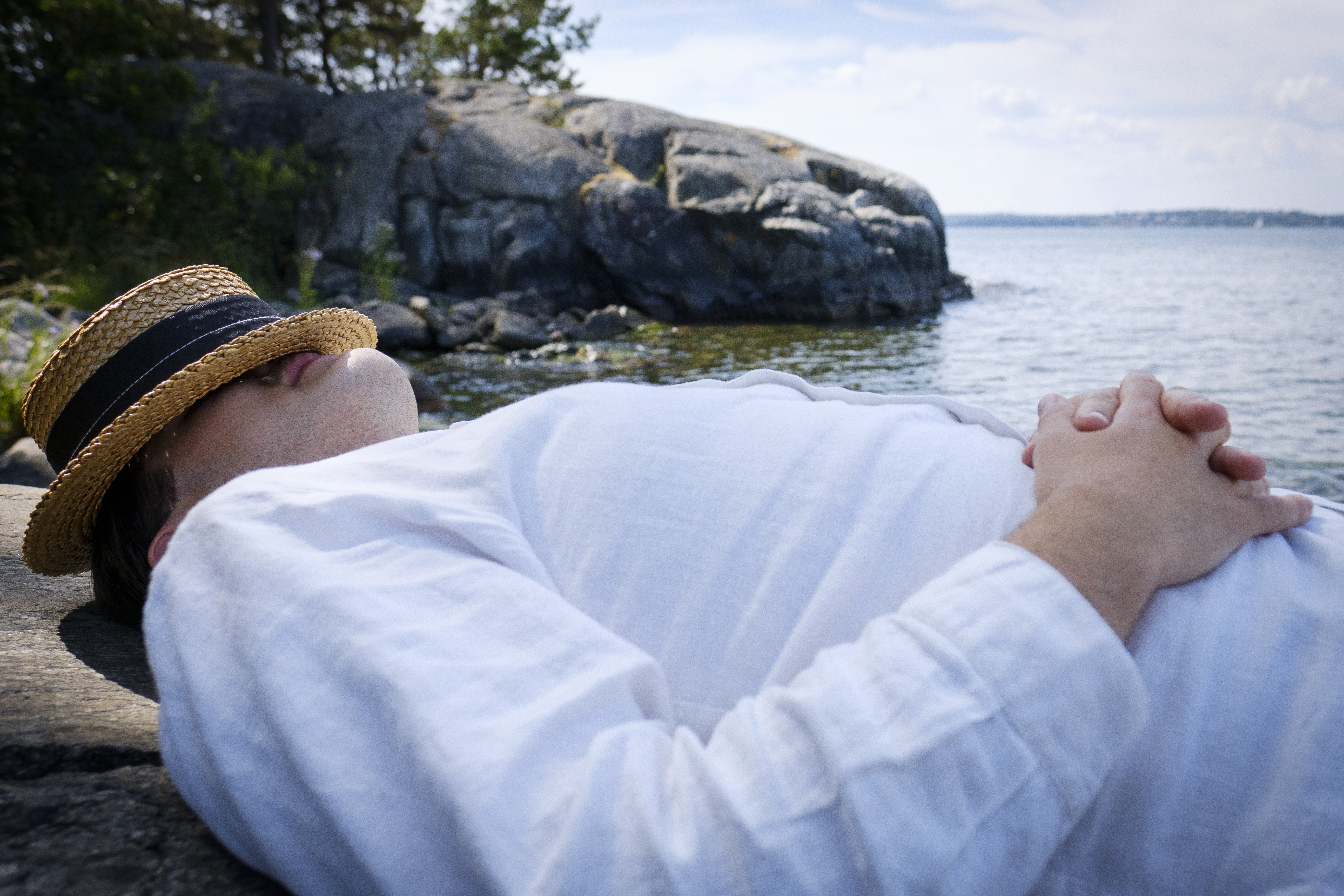 En man ligger och vilar på en klippa vid vattnet med hatten för ansiktet.