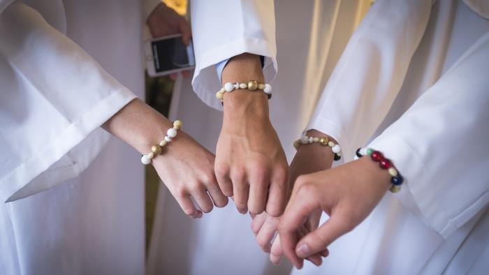 Några konfirmander med likadana pärlarmband sträcker fram händerna.
