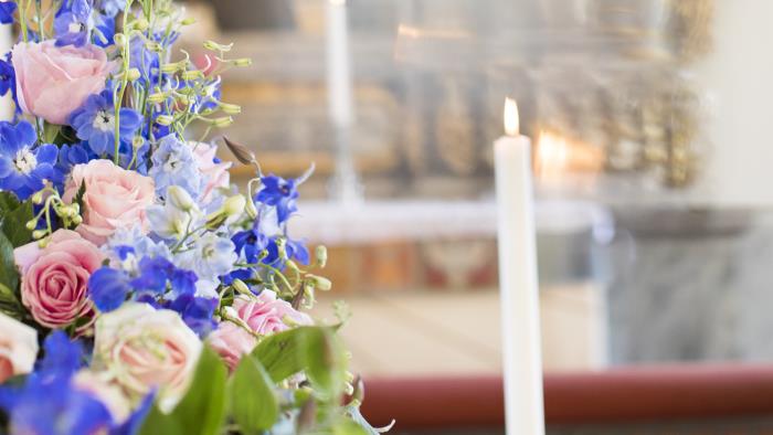 En begravningsbukett med skära och blå blommor ligger på en kista i en kyrka.