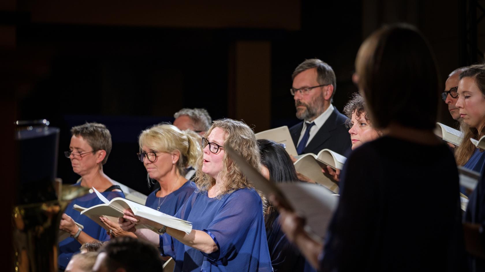 En blandad kyrkokör i matchande blå färger sjunger.