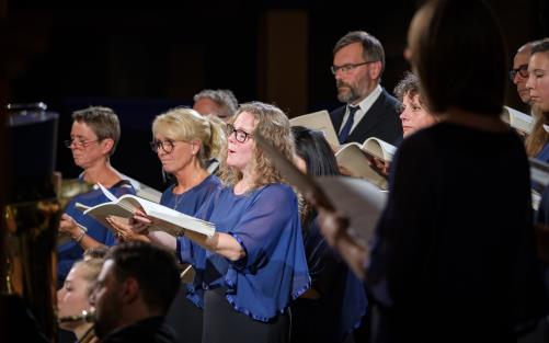 En blandad kyrkokör i matchande blå färger sjunger.