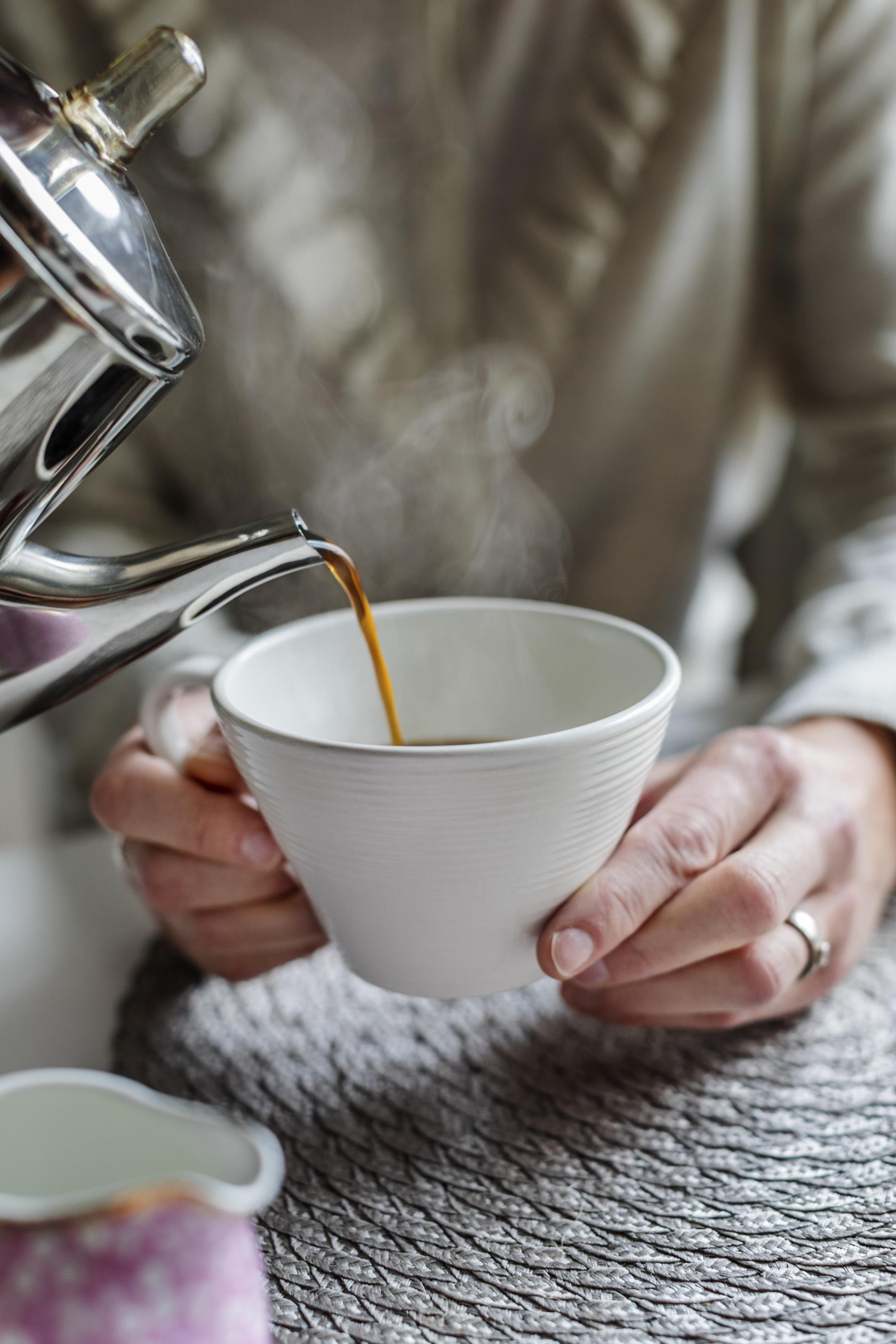 En person häller upp kaffe till någon som håller upp sin kopp.