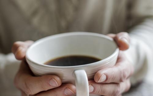 Någon håller händerna runt en kopp med kaffe.