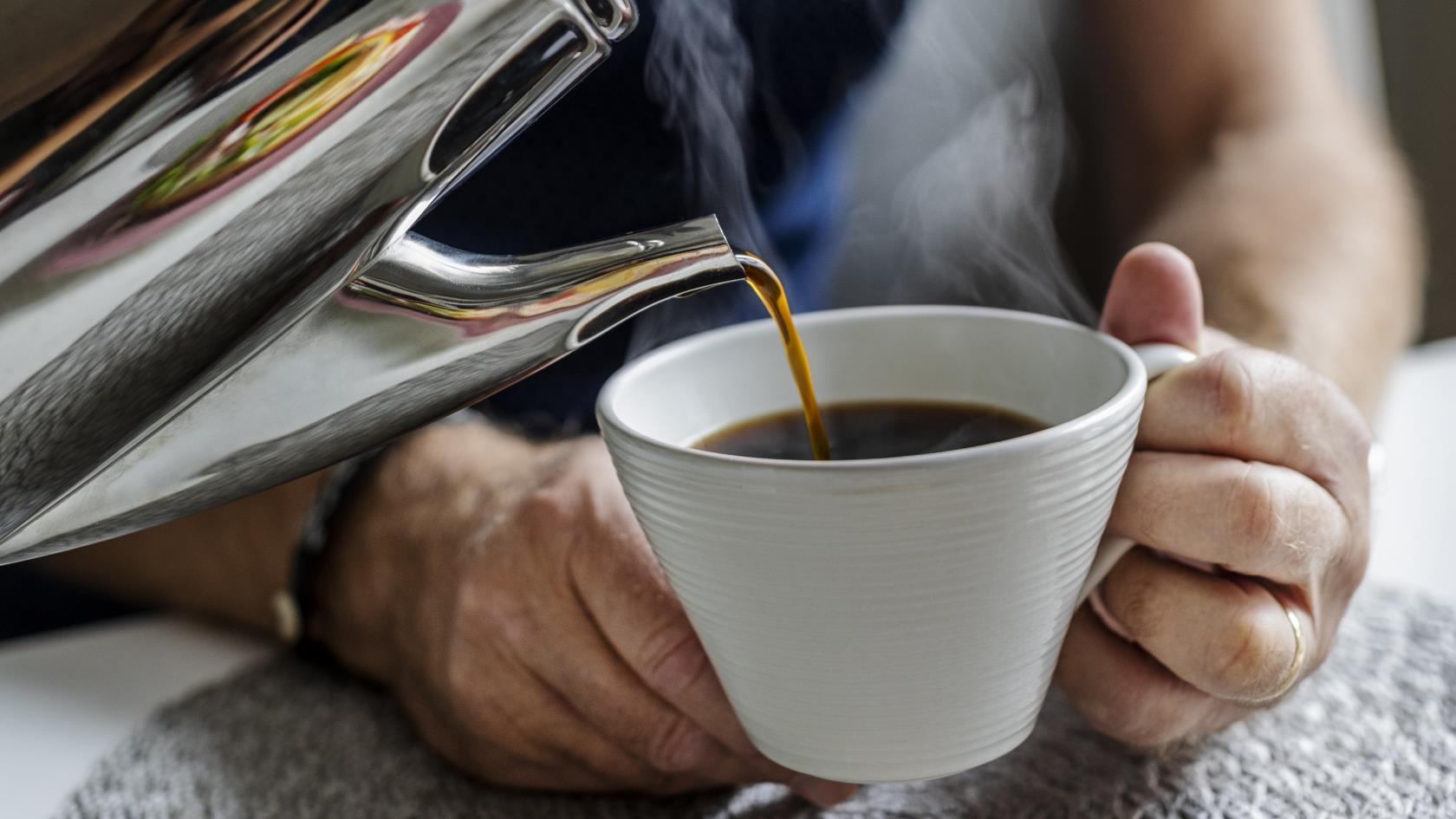 Någon häller upp kaffe till en man som sitter vid köksbordet.